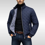 Man wearing a navy diamond-quilted jacket unzipped, revealing the soft grey fleece lining over a black polo neck
