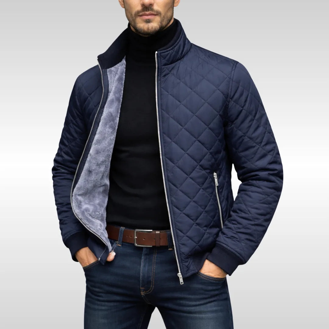 Man wearing a navy diamond-quilted jacket unzipped, revealing the soft grey fleece lining over a black polo neck