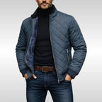 Front view of the steel-blue quilted jacket worn open, showing the stand collar and zip-up chest pocket