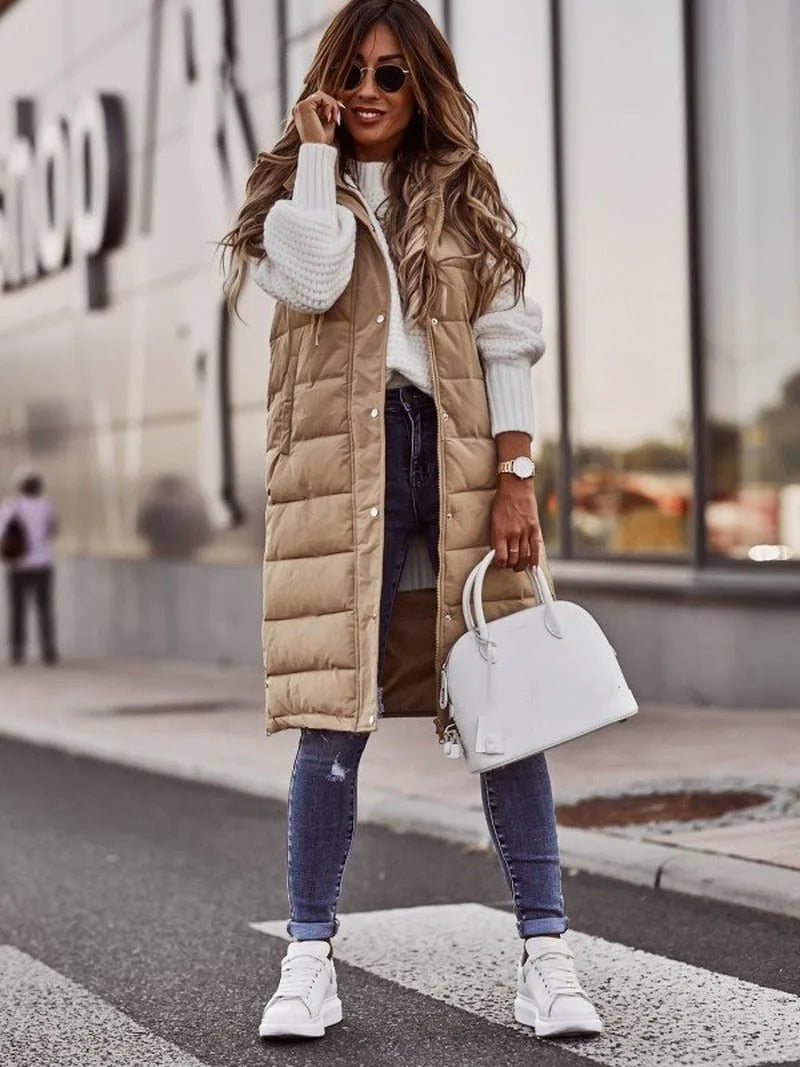 Woman wearing a beige longline quilted gilet over a chunky white knit jumper and skinny jeans