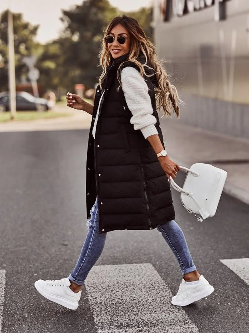 Woman walking in a black hooded quilted gilet paired with cuffed jeans and white trainers