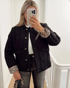 Woman wearing a black quilted jacket with leopard print cuffs, standing open over a white top and jeans