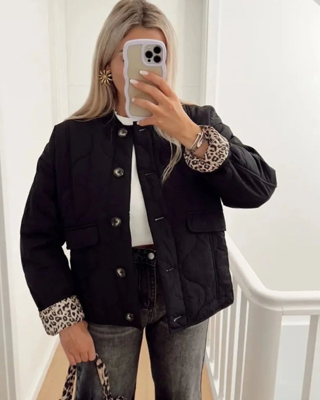 Woman wearing a black quilted jacket with leopard print cuffs, standing open over a white top and jeans