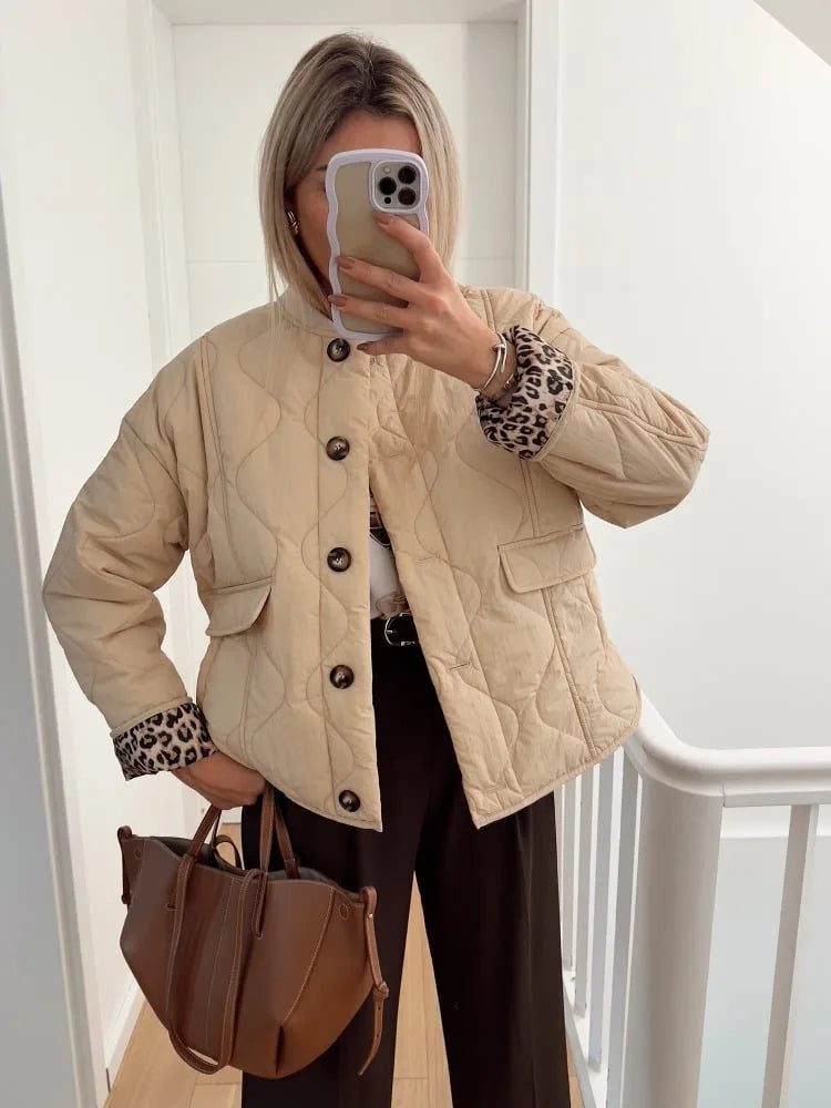 Beige quilted jacket with leopard lining worn open over a white top and dark brown trousers, holding a tan bag