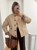 Beige quilted jacket with leopard lining worn open over a white top and dark brown trousers, holding a tan bag