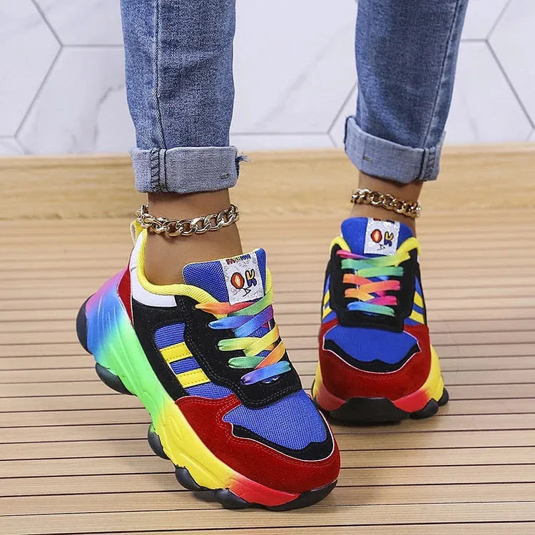 Side view of blue, red and black chunky trainers with rainbow gradient sole and tie-dye laces, worn with rolled-up jeans
