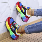Back view of blue and red chunky trainers against a white hexagon tile wall, showing the gradient rainbow heel