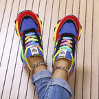 Top-down view of blue and red chunky trainers with tie-dye laces and rainbow sole, feet close together