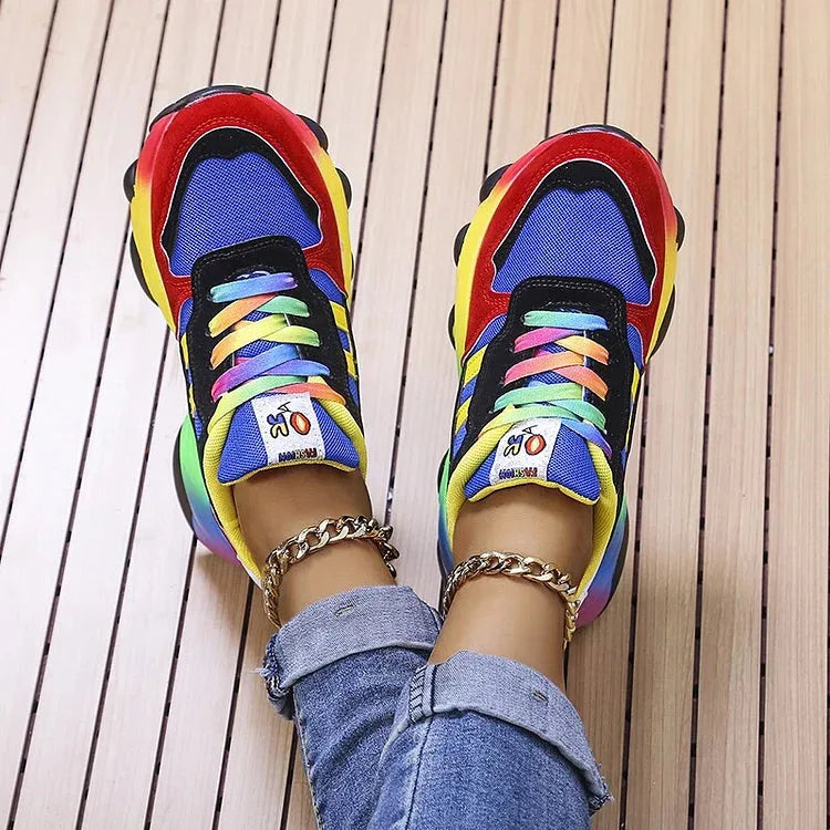Top-down view of blue and red chunky trainers with tie-dye laces and rainbow sole, feet close together