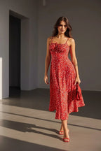 Woman walking in a red ditsy floral midi dress with thin straps, paired with red heeled sandals and a red bag