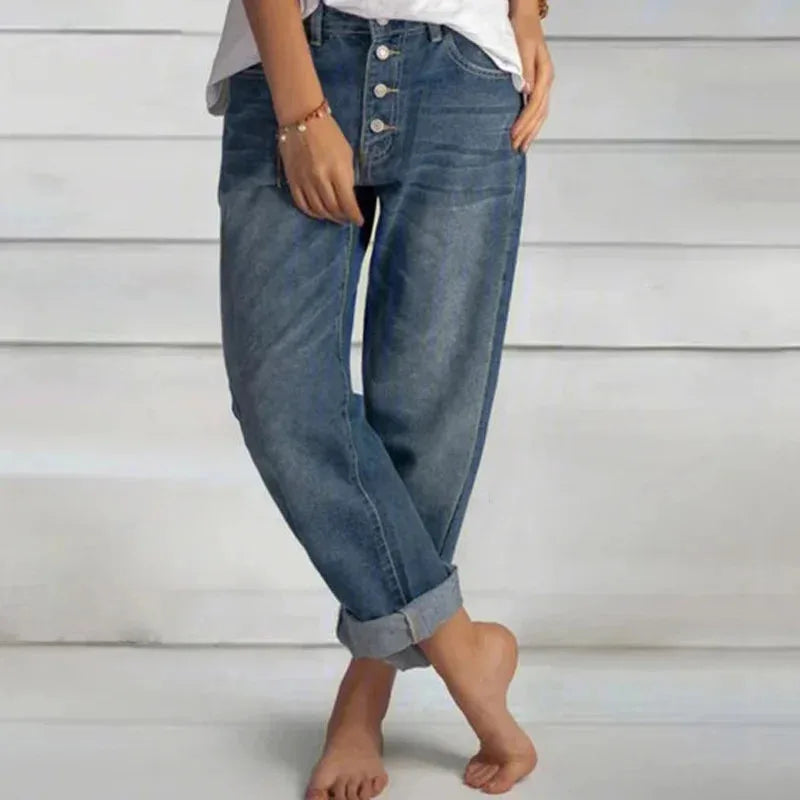 Side view of relaxed-fit blue denim jeans with button-fly waistband and cuffed hems, worn with a white tee