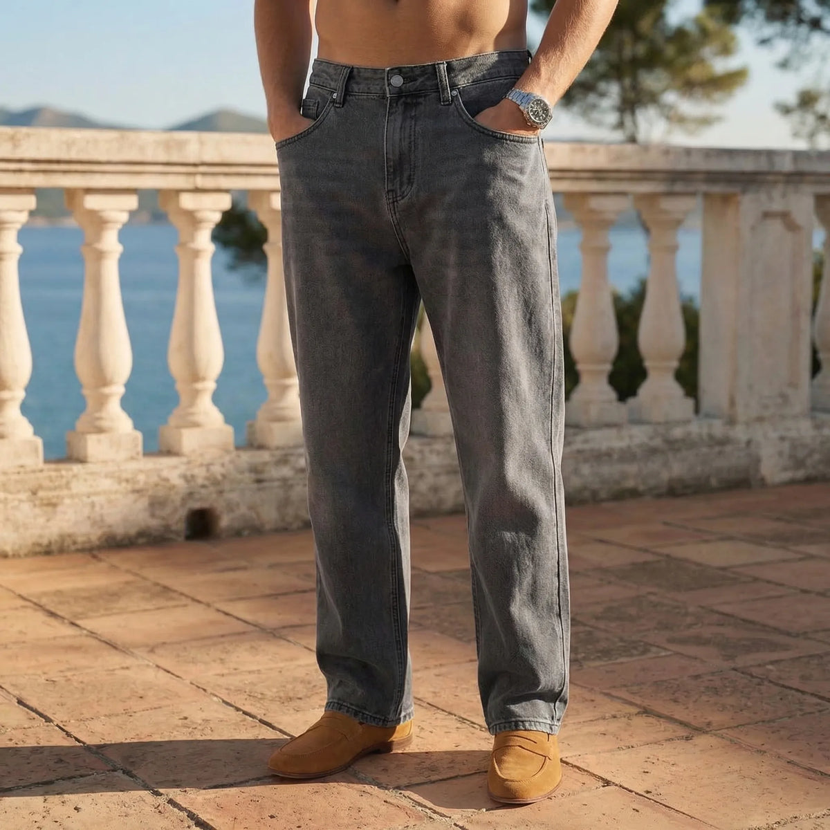 Front view of grey washed denim jeans with a relaxed straight cut, shown against a stone balustrade backdrop