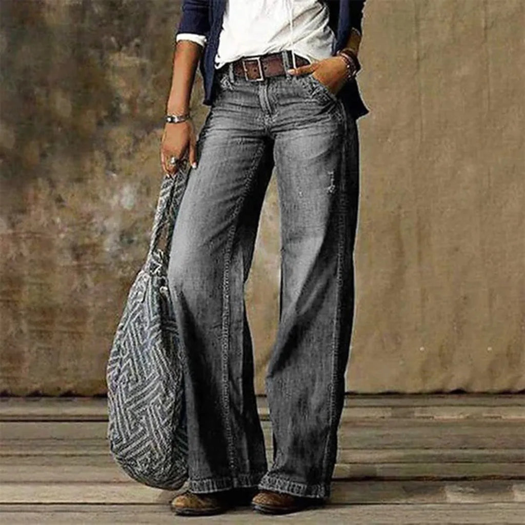 Light grey wash wide-leg jeans worn with a woven crossbody bag and brown leather boots