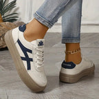 Pair of white trainers with bold navy side stripes and tan soles, one worn and one held outdoors