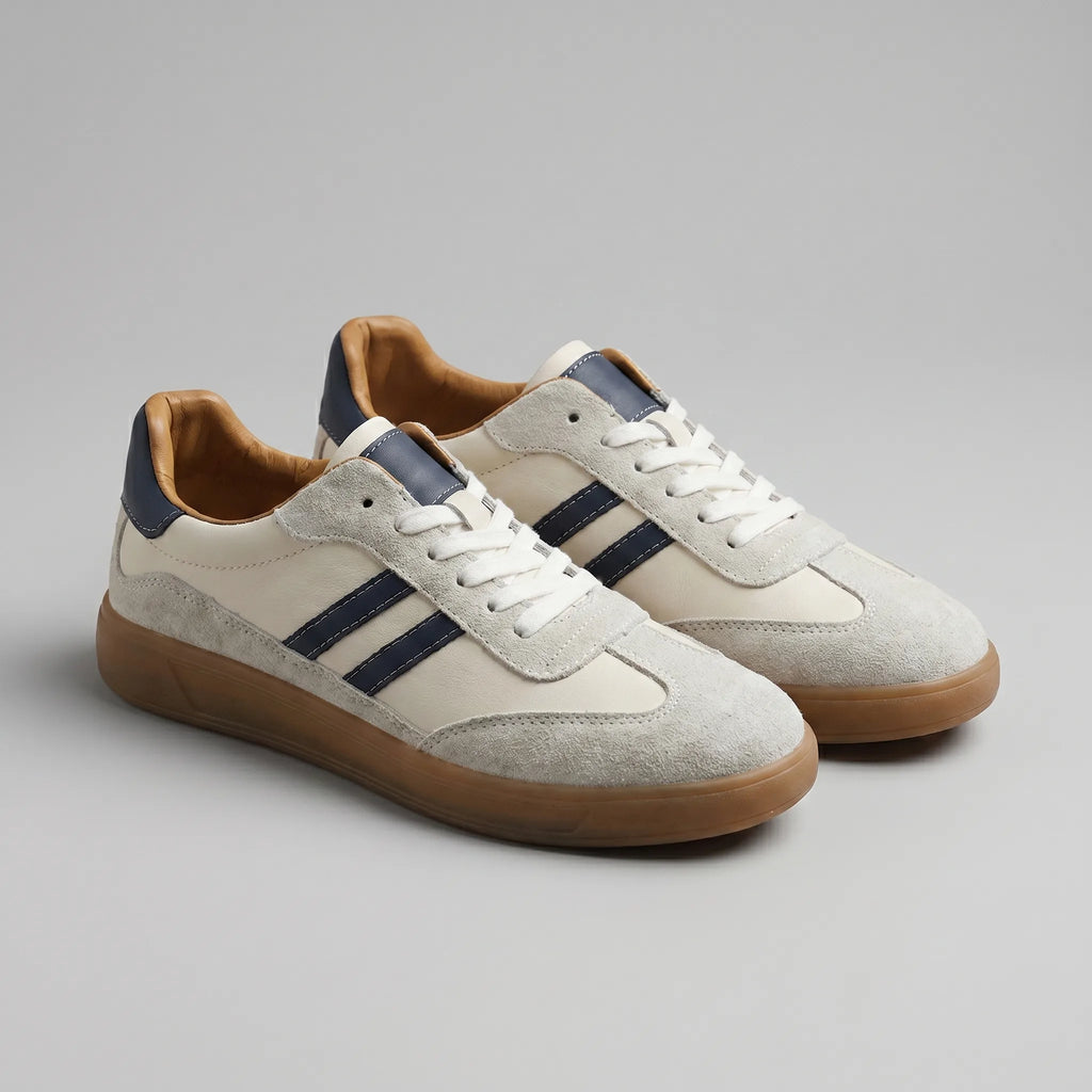 Angled front view of cream leather trainers with navy stripes, suede toe caps and gum rubber soles