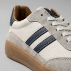 Close-up of the stitched navy leather stripes, suede toe panel and white laces on the shoe upper