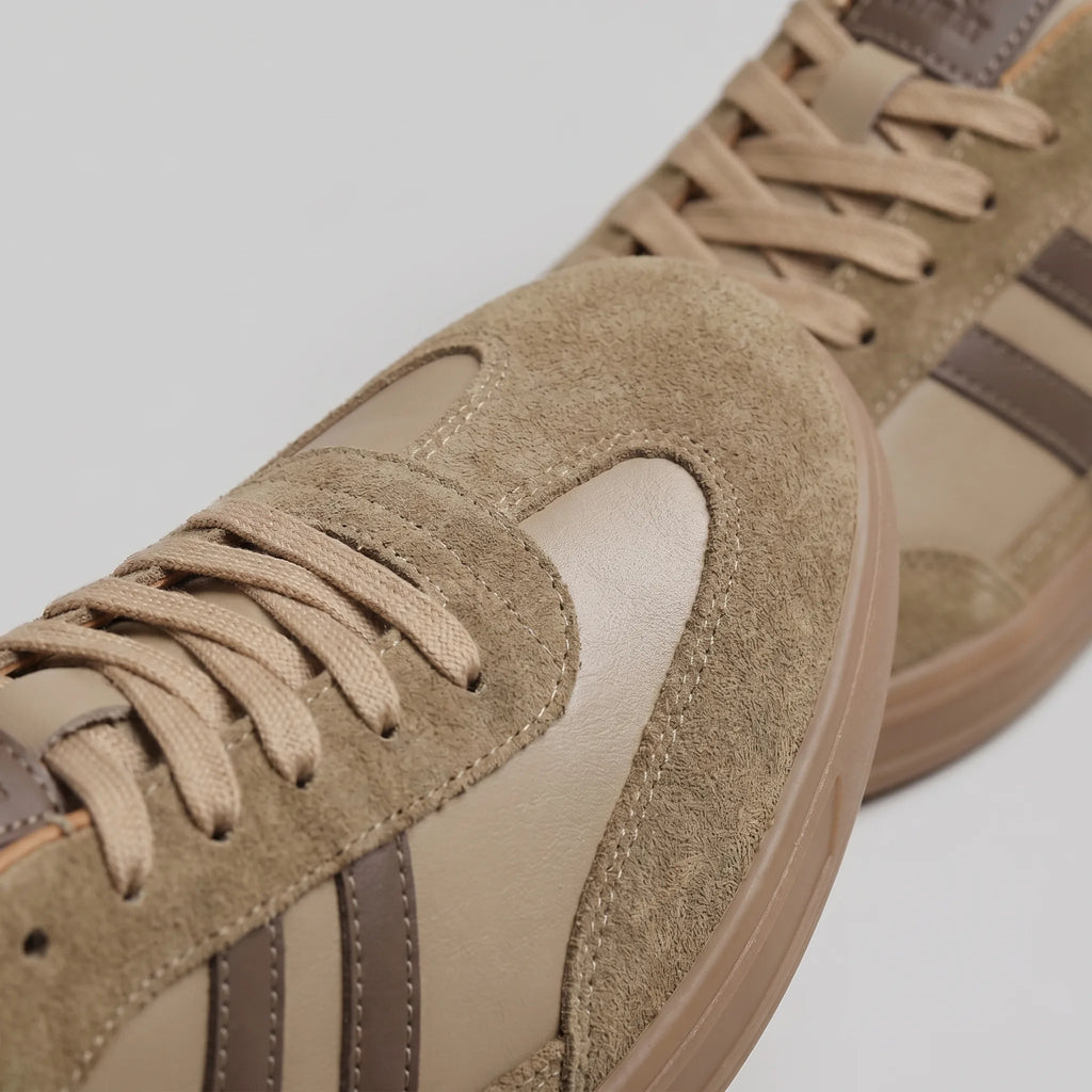 Three-quarter view of taupe trainers resting on a plain background, showing the full silhouette