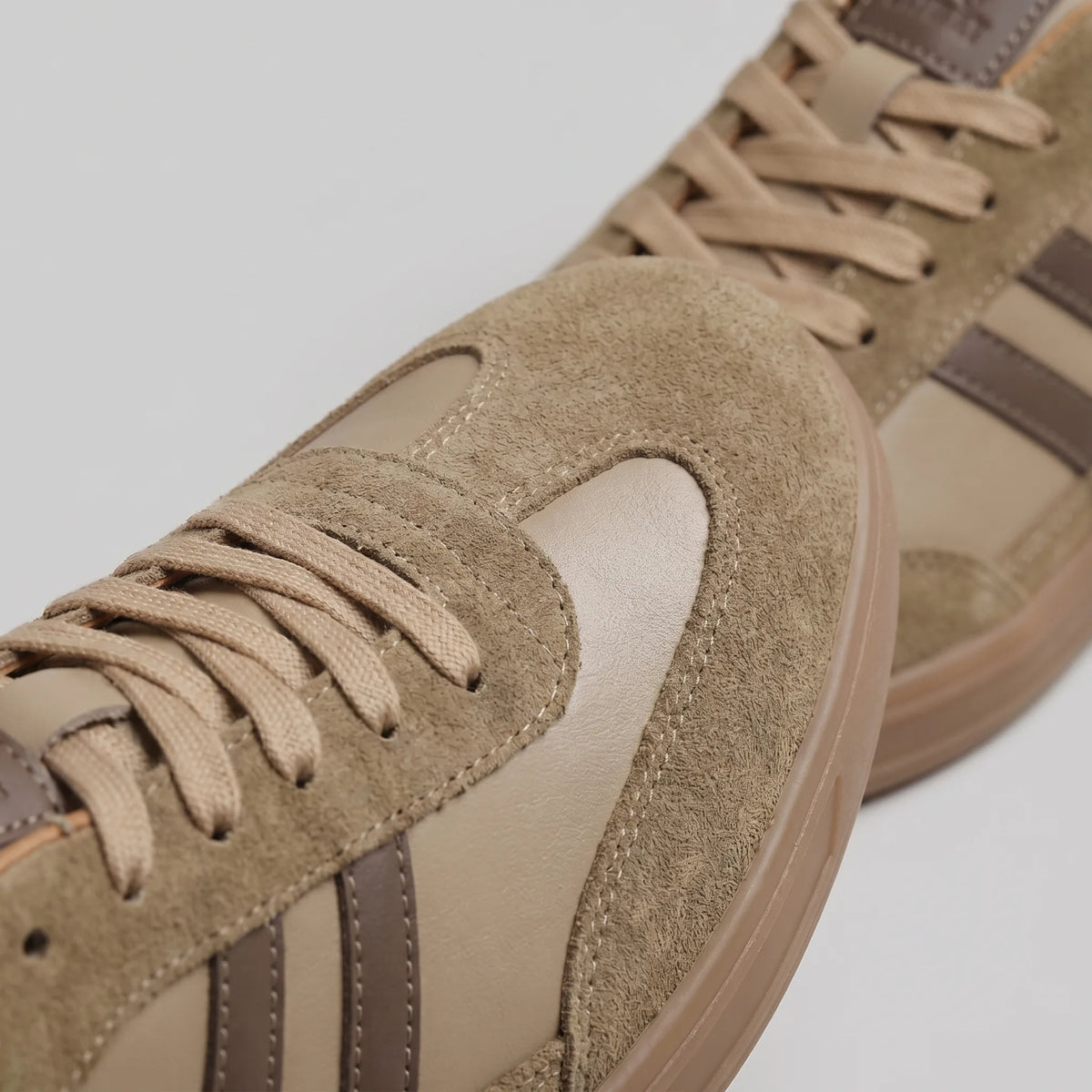 Three-quarter view of taupe trainers resting on a plain background, showing the full silhouette