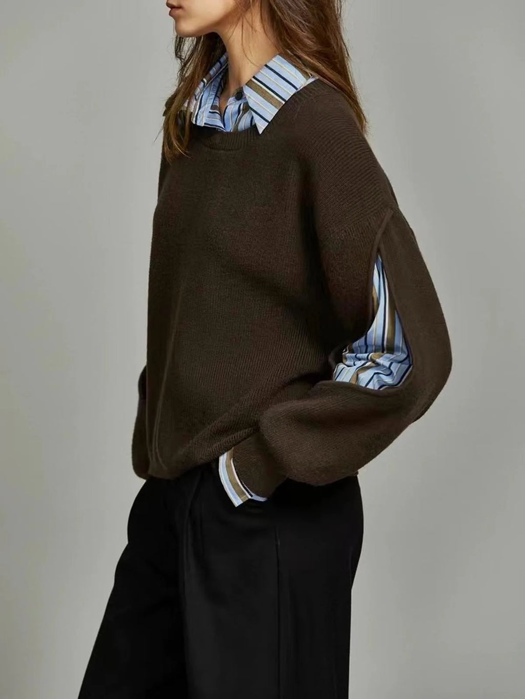 Side profile showing the dark brown knit jumper's dropped shoulder and cut-out sleeve revealing the striped shirt underneath