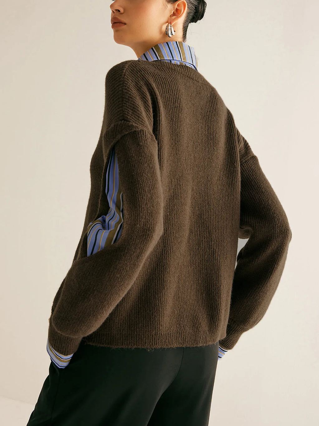 Back view of the dark brown ribbed jumper showing the relaxed fit and striped shirt sleeve through the cut-out
