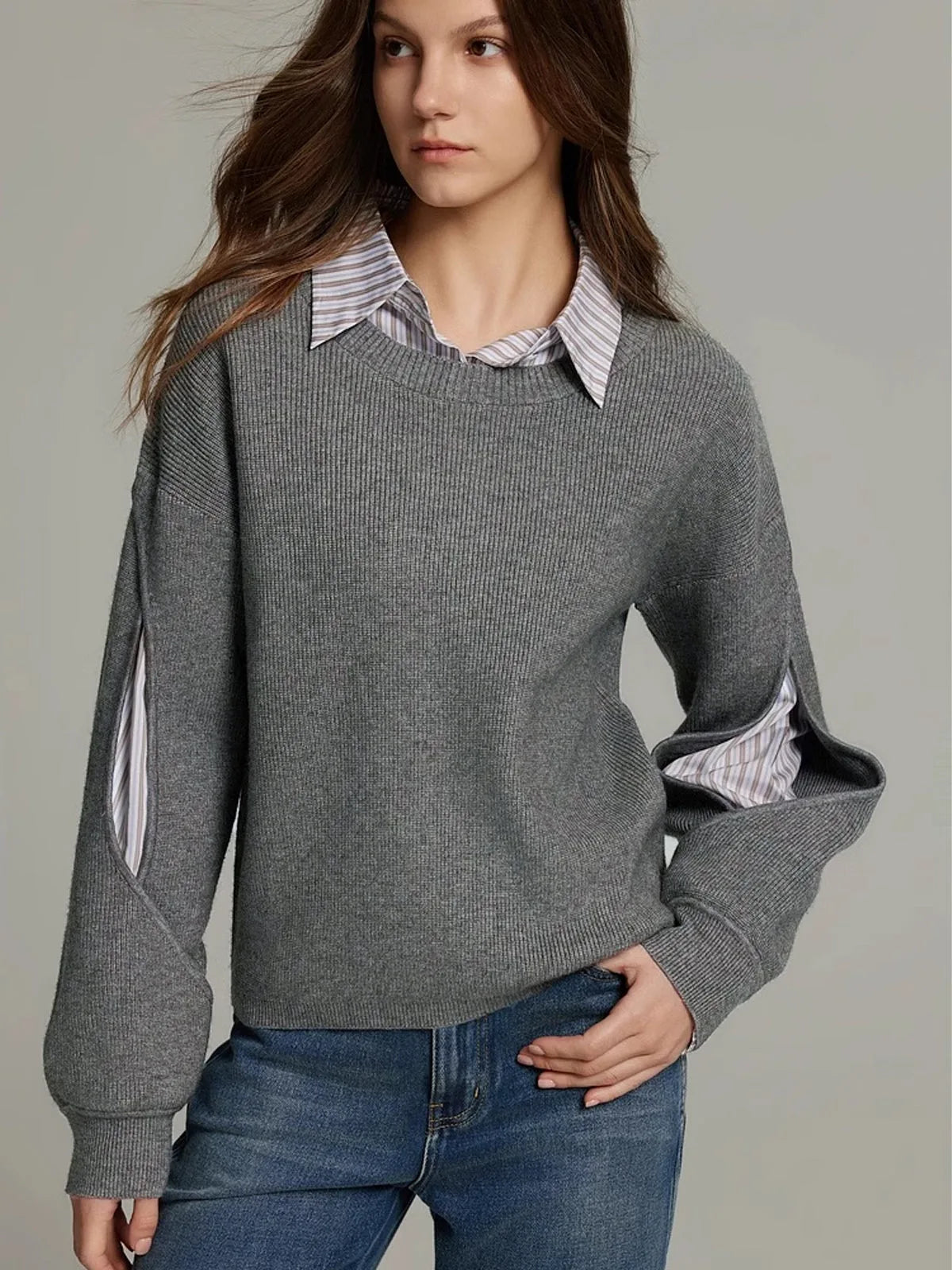 Grey knit jumper close-up showing the cut-out sleeve detail with the striped shirt visible underneath