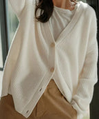 Close-up of white ribbed cardigan worn open over a white top and tan trousers, showing knit texture and buttons