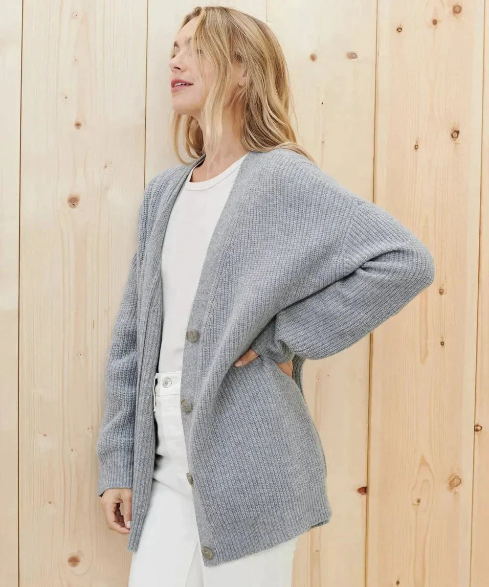 Side profile of grey ribbed cardigan worn over a white top and white trousers, showing oversized sleeve and hem