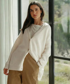 Woman in white ribbed cardigan standing by a window, worn over a white top and tan wide-leg trousers