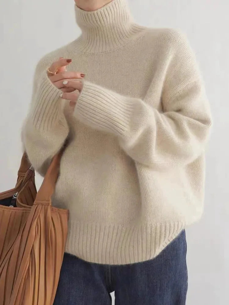 Close-up of an oversized beige roll neck jumper with ribbed cuffs, worn with a tan pleated shoulder bag