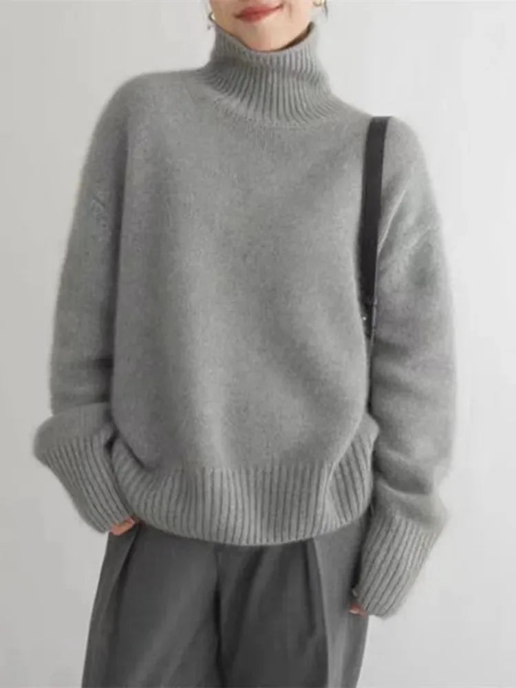 Smiling model wearing a grey polo neck jumper with a crossbody bag over the shoulder