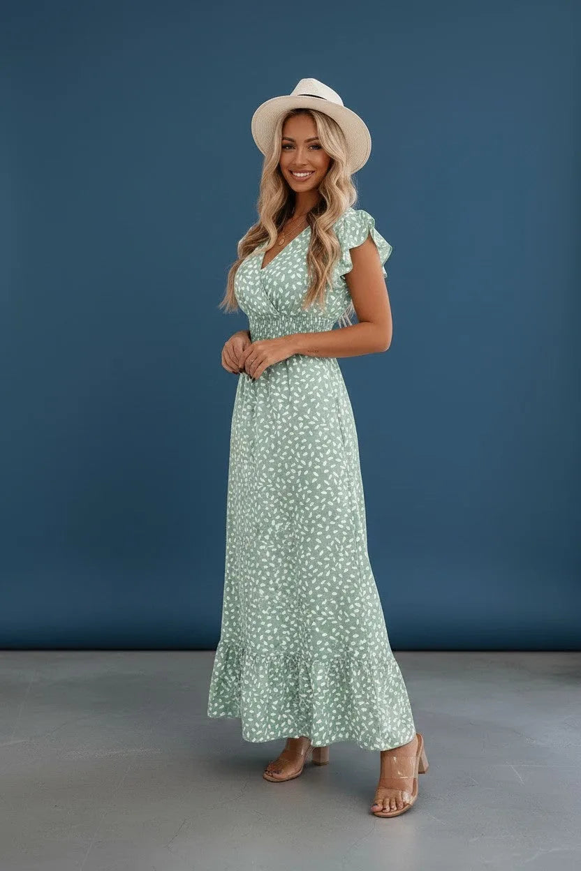 Side view of the sage green floral maxi dress showing the smocked waist and flowing A-line skirt against a blue backdrop