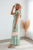 Back view of the maxi dress highlighting the smocked waist detail and tiered ruffle hem, paired with a beige handbag