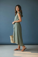 Side profile view of the sage green tie-waist dress showing the high-low asymmetric hem and flowing skirt movement.