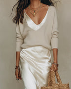 Close-up of an ivory satin cami dress layered under a cream ribbed V-neck jumper, worn with layered gold necklaces