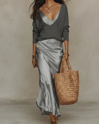 Grey satin slip skirt with a soft sheen worn under a charcoal grey ribbed V-neck jumper, styled with a straw tote bag