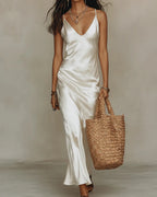 Close-up front view of an ivory satin cami dress with a V-neckline, worn alone under a cream jumper draped off the shoulders