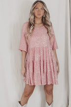 Pink sequin tiered mini dress with three-quarter sleeves and a round neckline, styled with layered necklaces and boots