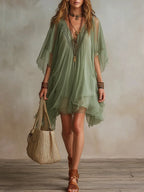 Woman walking in a sage green sheer tunic dress with flowing batwing sleeves, holding a woven straw tote bag