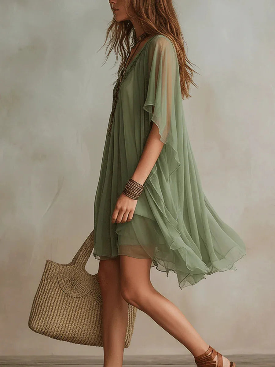 Side profile view showing the loose flowing silhouette and layered hemline of the green sheer tunic dress in motion