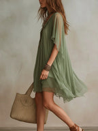 Side profile view showing the loose flowing silhouette and layered hemline of the green sheer tunic dress in motion