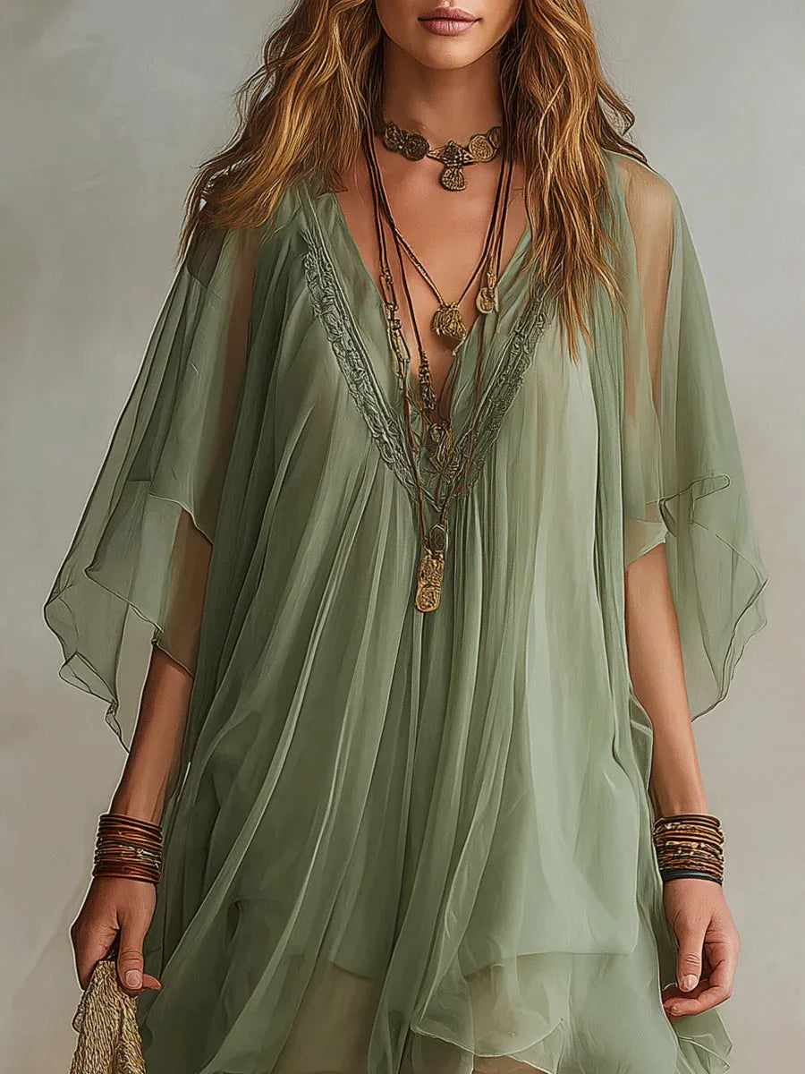 Detail shot of the V-neckline embroidery and sheer fluttering sleeves against layered gold necklaces