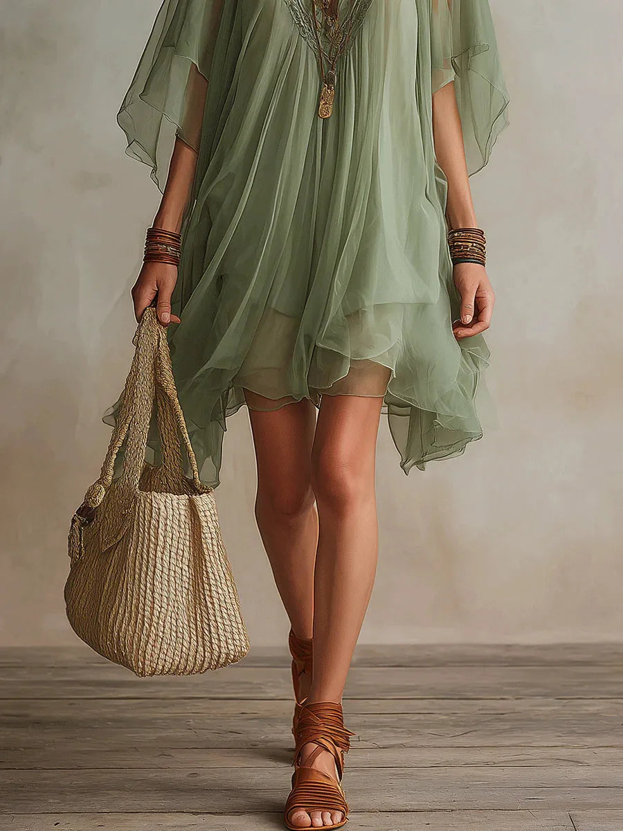 Close-up of the flowing chiffon skirt hemline paired with strappy tan sandals and a woven straw bag