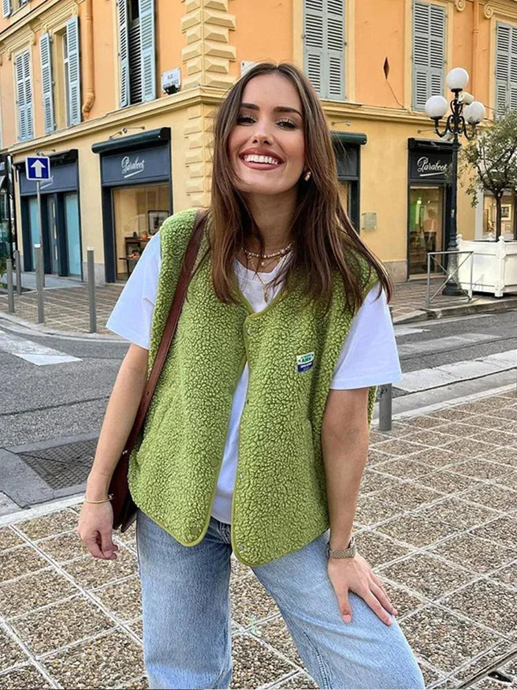 Woman wearing a cropped green sherpa fleece body warmer over a white t-shirt and jeans on a street corner