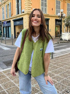 Woman wearing a cropped green sherpa fleece body warmer over a white t-shirt and jeans on a street corner