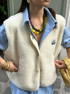 Close-up of the cream sherpa fleece body warmer collar and snap buttons worn over a striped shirt
