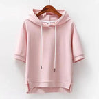 Pink short-sleeve drawstring hoodie on a wooden hanger, showing the relaxed hood and high-low hem