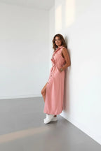 Side profile of the sleeveless denim dress leaning against a wall, highlighting the A-line skirt length and tie belt detail.