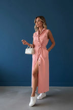 Woman walking in the blush pink denim shirt dress carrying a white handbag, showing the flowing skirt and side split in motion.