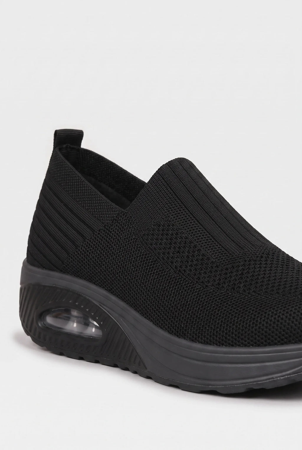 Close-up angled view of black knit slip-on trainer showing ribbed texture and pull tab at the heel