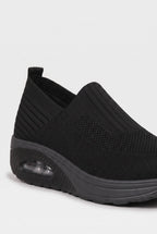 Close-up angled view of black knit slip-on trainer showing ribbed texture and pull tab at the heel